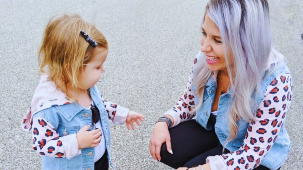 A woman and a young girl sit on the ground, engaged in a simple daily schedule activity for a 2-year-old.