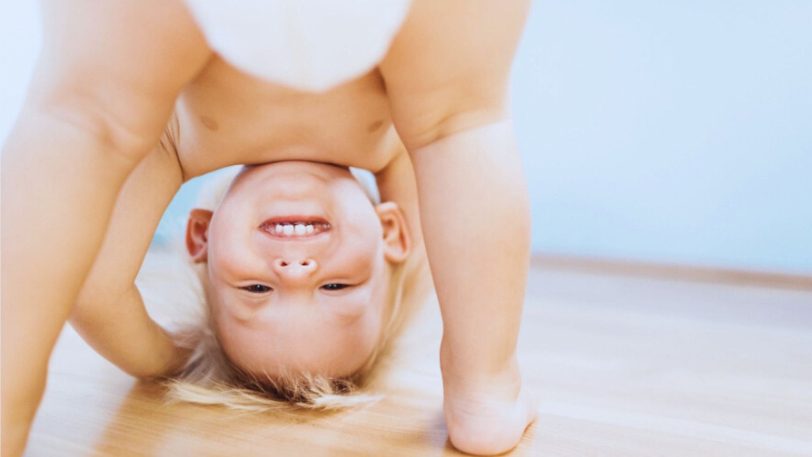 A young child is playfully upside down on a wooden floor, illustrating the playful nature of the 2 to 1 nap transition.
