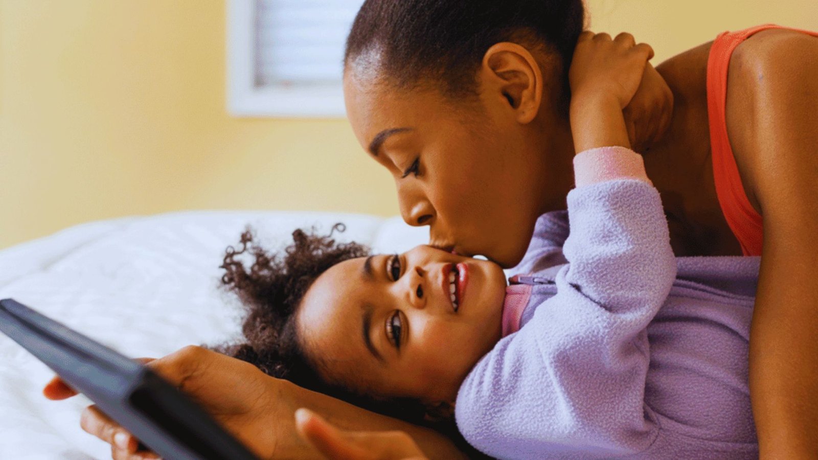 A woman and a child relax together on a bed, illustrating a cozy bedtime routine.
