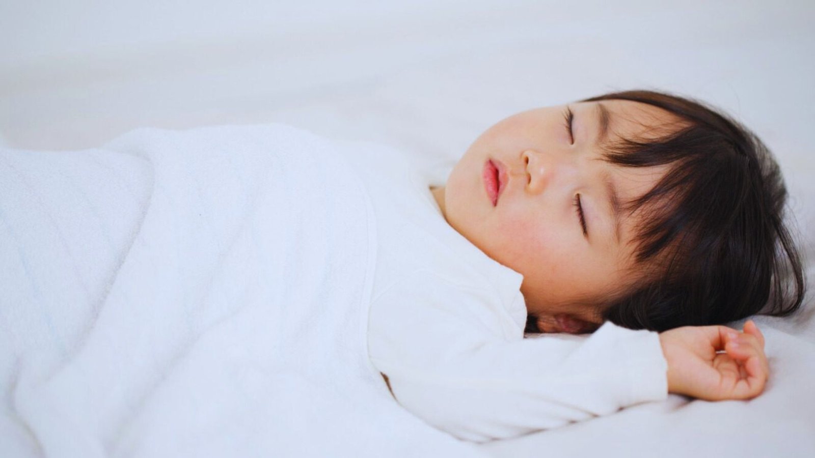 A peaceful baby sleeping on a bed with white sheets, illustrating a serene nap environment during the 2 to 1 nap transition.