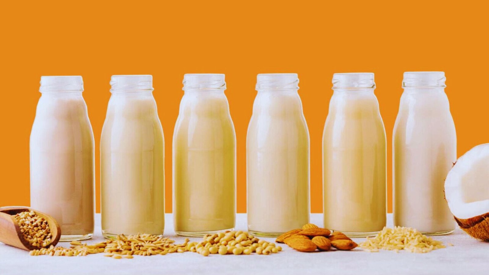  Five bottles of milk and a bowl of nuts arranged neatly on a wooden table.