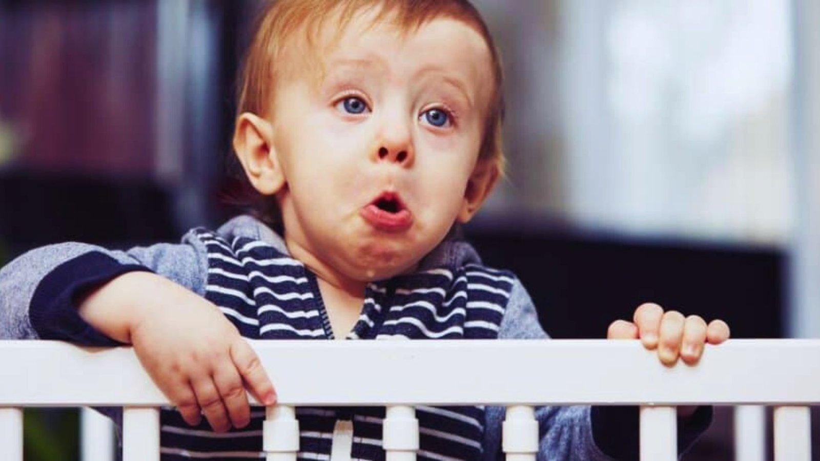 A baby leaning over a railing, sticking out his tongue, embodying the stressful spirit of toddler bedtime.
