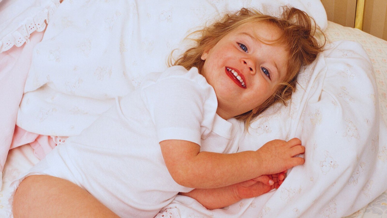 A smiling little girl lying on a bed, showcasing joy and comfort during bedtime.