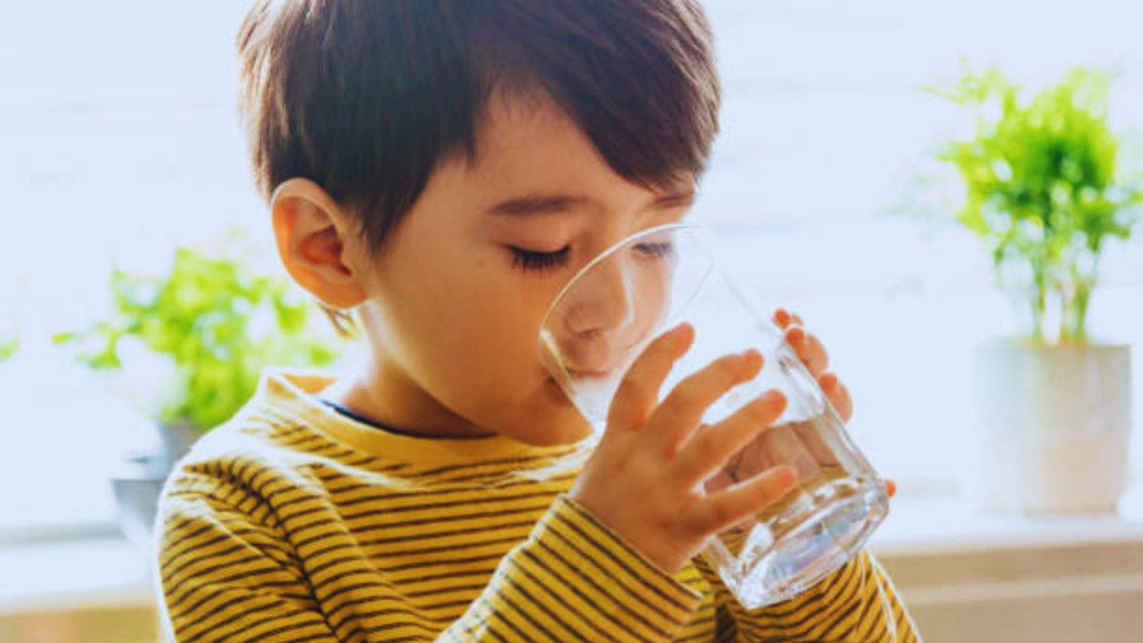 A young boy happily drinking water from a clear glass, showcasing a moment of refreshment and hydration.
