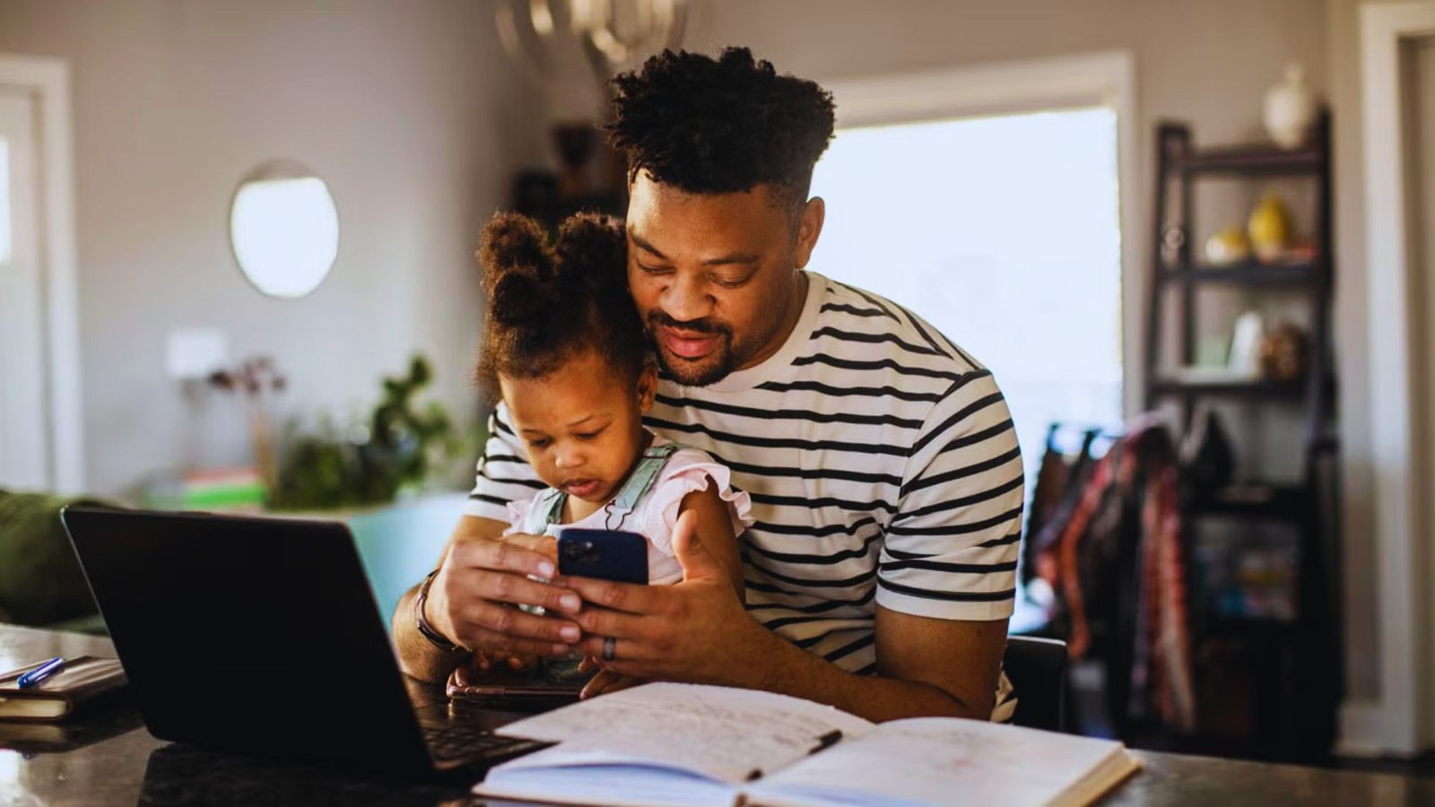 A man and a child engaged with a laptop in a room, discussing a daily schedule for a 2-year-old at home.
