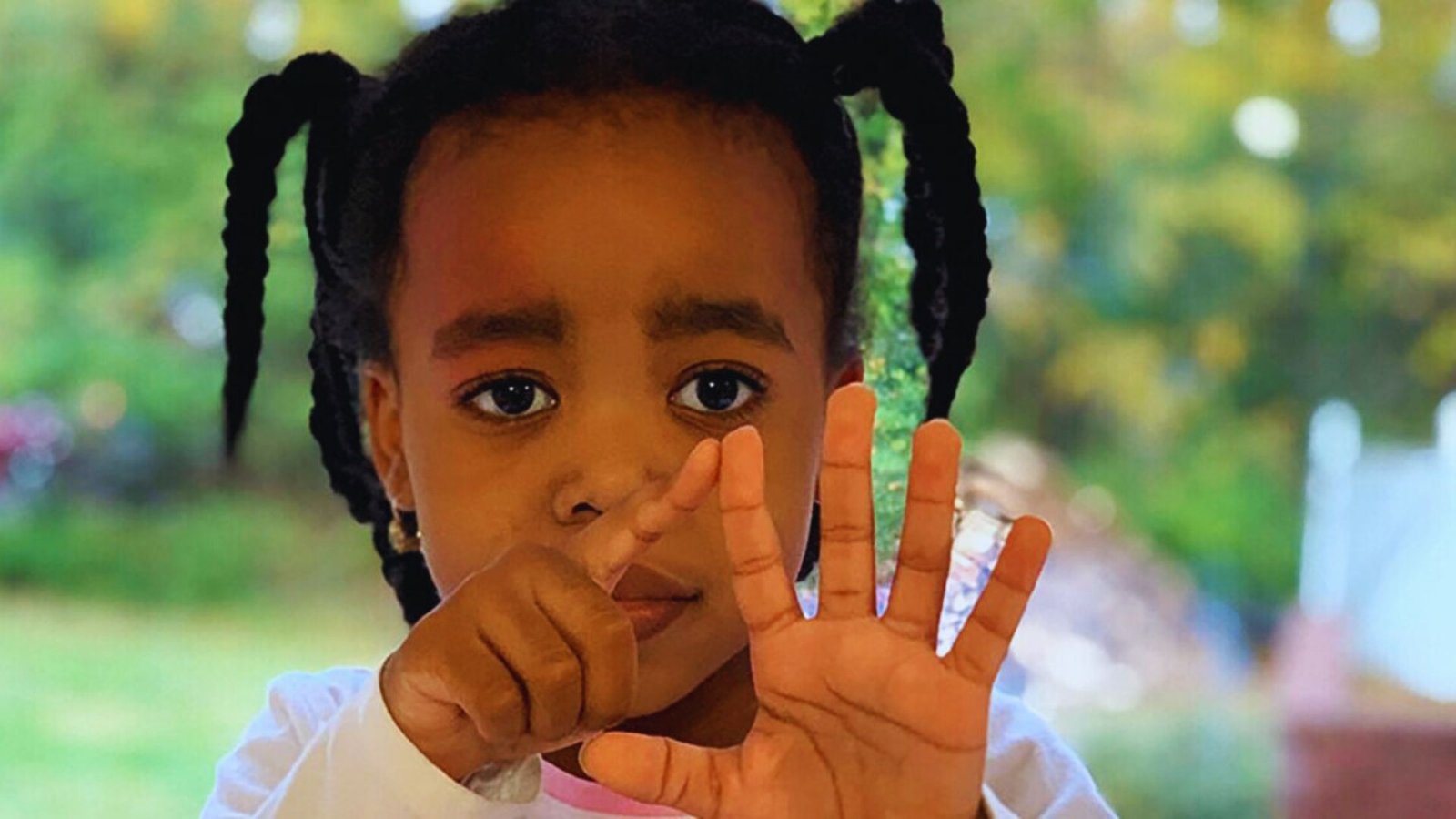  A young girl with braids is making a hand gesture, smiling and looking directly at the camera.
