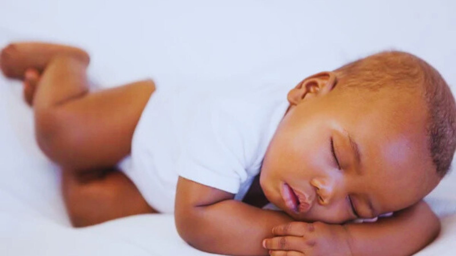 A peaceful baby sleeping on a white bed, illustrating the importance of understanding sleep patterns for parents.
